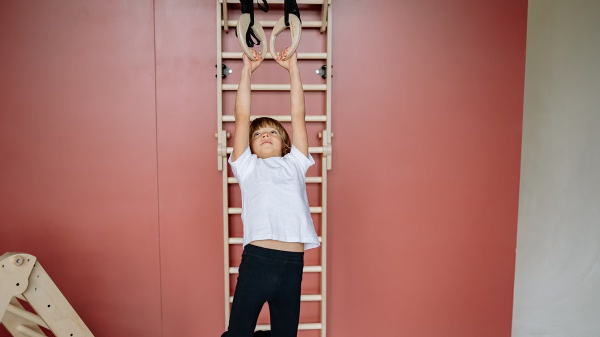 Young boy having fun and building strength on indoor gym rings at home.
